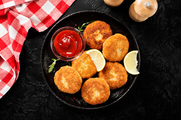 Chicken patties or fish cakes fried in breadcrumbs with ketchup and lemon slices. black  background, top view