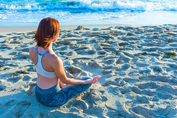 Yogi young person practicing yoga on the beach - In sportive top and leggings
sitting in Ardha...