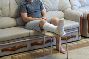 The guy is sitting on the couch in a cast. The leg is in a cast.