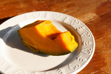 Steamed pumpkin on white plate with warming sunlight; healthy food on wooden table.