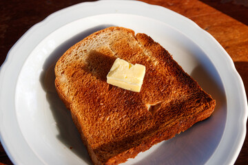 Toasted bread and butter with morning sunlight. Overhead shot of a piece of buttered toast.