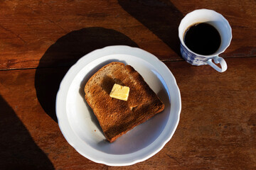 Toasted bread and butter with black coffee. Overhead shot of a breakfast with beautiful morning sunlight.