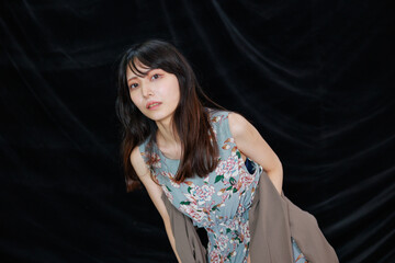 黒背景の前でポーズする袖なしワンピースのセクシーな日本人女性