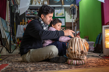 a small child learning to play the tabla from the teacher