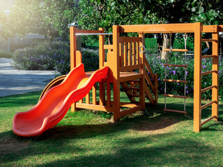 Kids playground equipment for children with orange color slide and wood and rope ladder in the yard with no people.