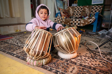 a small child trying to learning to play the tabla . - obrazy, fototapety, plakaty