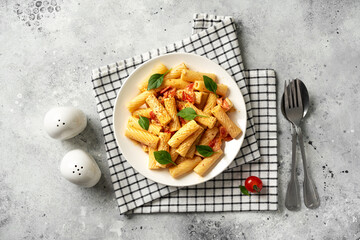 Tortiglioni with tomatoes, ricotta and basil in a white plate on a light kitchen table. Traditional Italian pasta with vegetables and creamy cottage cheese in a bowl. Top view