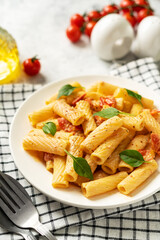 Tortiglioni with tomatoes, ricotta and basil in a white plate on a light kitchen table. Traditional Italian pasta with vegetables and creamy cottage cheese in a bowl closeup