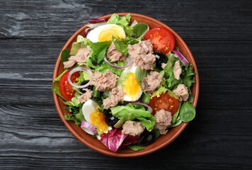 Bowl of delicious salad with canned tuna and vegetables on black wooden table, top view