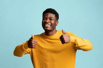 Cute black guy showing thumb ups, posing on blue background