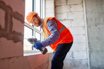 Builder in hardhat working with drill indoors