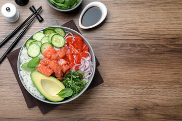 Delicious poke bowl with salmon and vegetables served on wooden table, flat lay. space for text