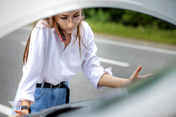 Young woman standing near broken down car with popped up hood having trouble with her vehicle....