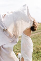 Fototapeta na wymiar A beautiful Caucasian girl on a summer day. A girl in a white dress runs across a field and plays with a handkerchief. A young carefree woman running towards the sun. Wind in her hair.