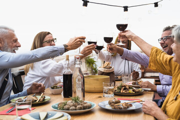 Multiracial senior friends dining together and toasting with red wine on house patio dinner - Food...