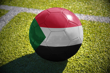 football ball with the national flag of sudan lies on the green field