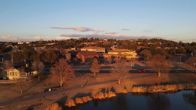 4k Aerial Drone footage of a small park in Arizona at golden hour with slow camera pullback motion revealing a pond with a water fountain and a fishing dock, Cinematic