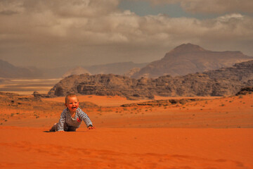 A cute baby girl crawling on a sand. Wadi Rum desert and mountains, Jordan.