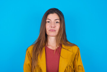 young brunette woman wearing yellow fringed jacket over blue background crying desperate and depressed with tears on his eyes suffering pain and depression. Sad facial expression and emotion concept.