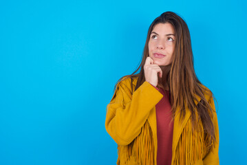 Portrait of thoughtful young caucasian woman wearing yellow fringed jacket over blue keeps hand...