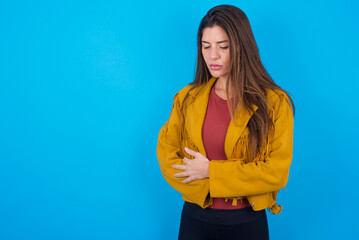 young caucasian woman wearing yellow fringed jacket over blue background suffering from strong...