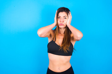 Fototapeta na wymiar Young beautiful sportswoman doing sport wearing sportswear over blue background holding head in hands with unhappy expression watching sad movie about animals and trying not to cry.