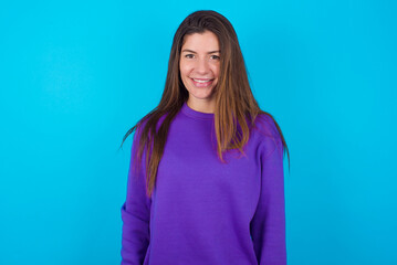 Fototapeta premium young caucasian woman wearing purple hoodie against blue background with nice beaming smile pleased expression. Positive emotions concept