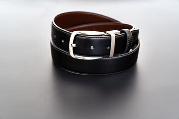 Double-sided black and brown leather belt with an unbuttoned buckle on a black background.