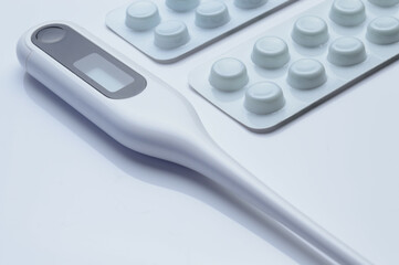 tablets in a package and a white electronic thermometer on a white surface close-up.