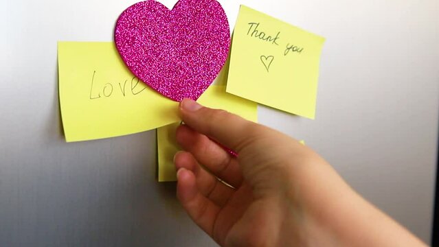 Declarations of love written on colored stickers pasted on the refrigerator at home. Women's hands are writing a letter. Valentine's Day.