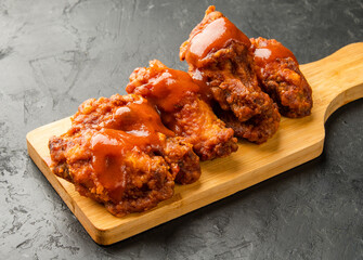 Bbq wings on a wooden board on a dark table. Wings covered in sauce.