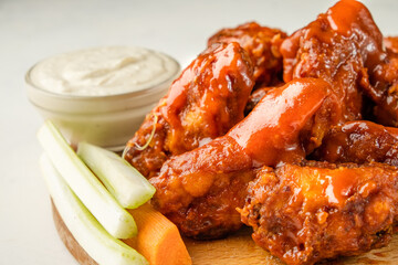 Buffalo wings close-up poured with sauce on a light table. Traditional appetizer of chicken wings.