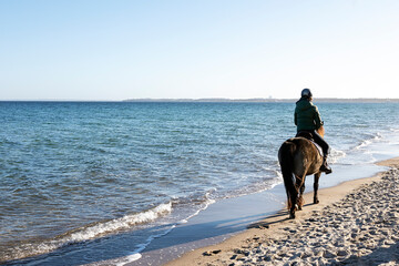 Eine junge Frau reitet am Strand, nahe der Brandung auf ihrem Pferd und sie genießen das Wetter