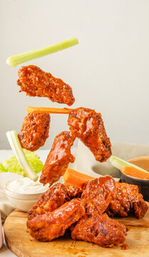 Falling chicken wings buffalo sauce with carrot and celery sticks. Fried bbq wings in flight. Traditional American cuisine concept.
