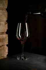 Close up perspective of dark bottle filling crystal clear wine glass with red wine