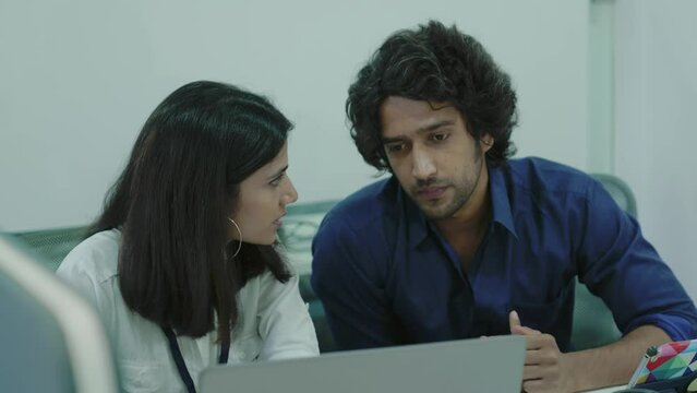 Indian Female manager insurer consulting male customer with laptop at meeting young Asian woman or mentor showing online presentation of deal benefits talking convincing client teaching intern office.