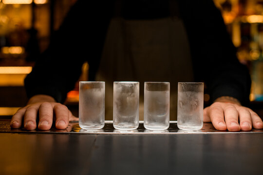 Bartender hands near four chilled shot glasses on the bar counter