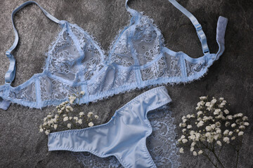 Elegant light blue women's underwear and gypsophila flowers on grey background, flat lay