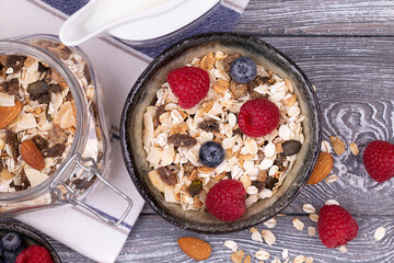Homemade granola with nuts, raspberries and blueberries, milk on a gray whitewashed rustic table, top view, copy space. Healthy breakfast