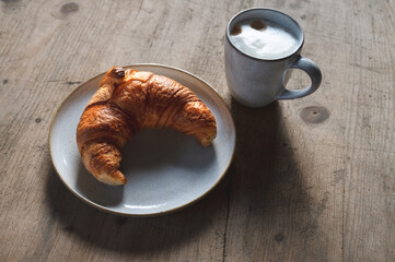 fresh golden brown croissant with a cappuccino on a stoneware plate and rustic wooden table