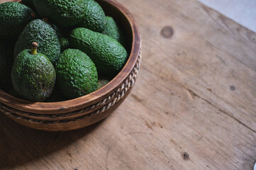 freshly harvested green avocados lie in a wooden bowl on a rustic wooden table