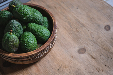 freshly harvested green avocados lie in a wooden bowl on a rustic wooden table