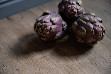 Obraz premium three fresh artichokes lie on a rustic wooden board asl healthy food
