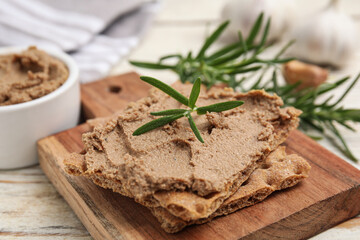 Fototapeta na wymiar Crispy crackers with delicious meat pate and rosemary on white wooden table, closeup
