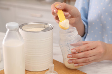 Woman preparing infant formula at table indoors, closeup. Baby milk