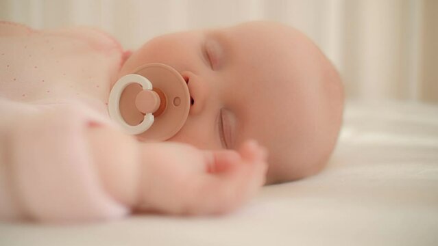 Close up face of adorable sleeping toddler lying on comfy white bed suck pacifier feeling calmness