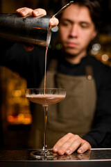 bartender professionally pours brown cocktail from shaker into glass