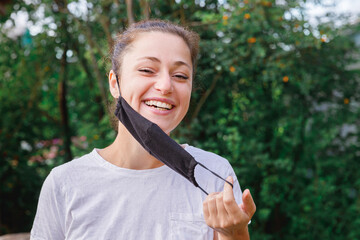Happy positive girl takes off protective medical mask from face outdoors. Young woman removing mask...