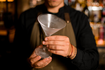 close-up photo of bartender in black t-shirt holding cooled empty martini glass