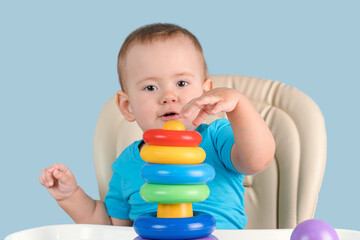 Joyful toddler 12-17 months old with his mouth open in surprise builds a pyramid tower of colored rings for the first time.